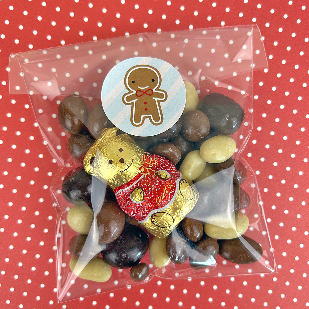 A clear gift bag full of nuts and chocolate sealed with a gingerbread man sticker