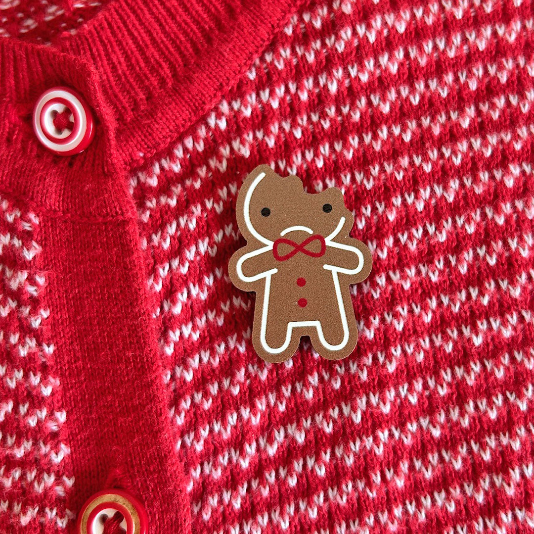 A sad kawaii Gingerbread Man brooch with the top of his head bitten off.
