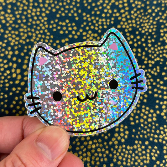 A die cut vinyl sticker of a kawaii cat showing the sparkly holographic glitter foil