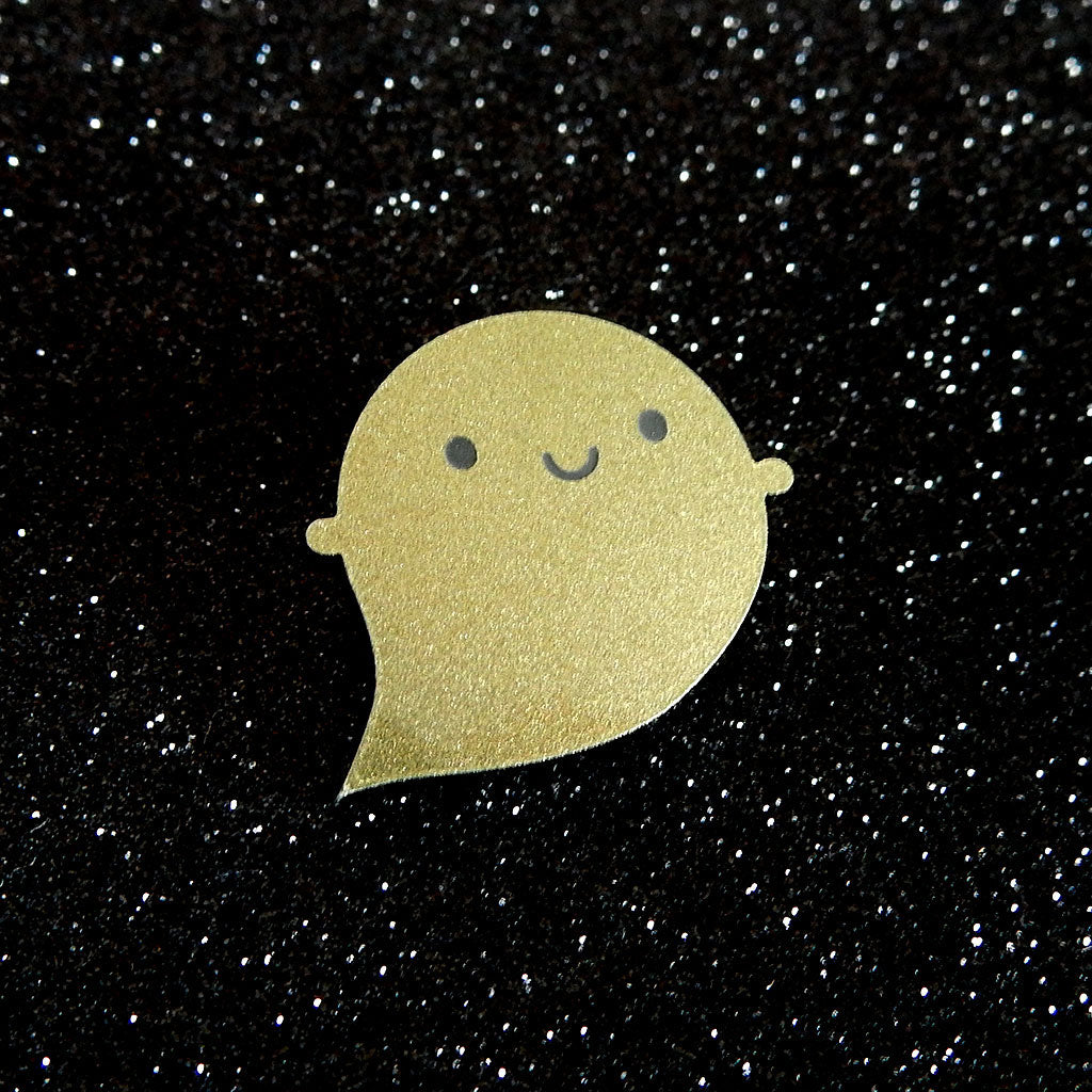 A Golden Ghost brooch photographed at an angle to catch the shimmer effect and engraved face
