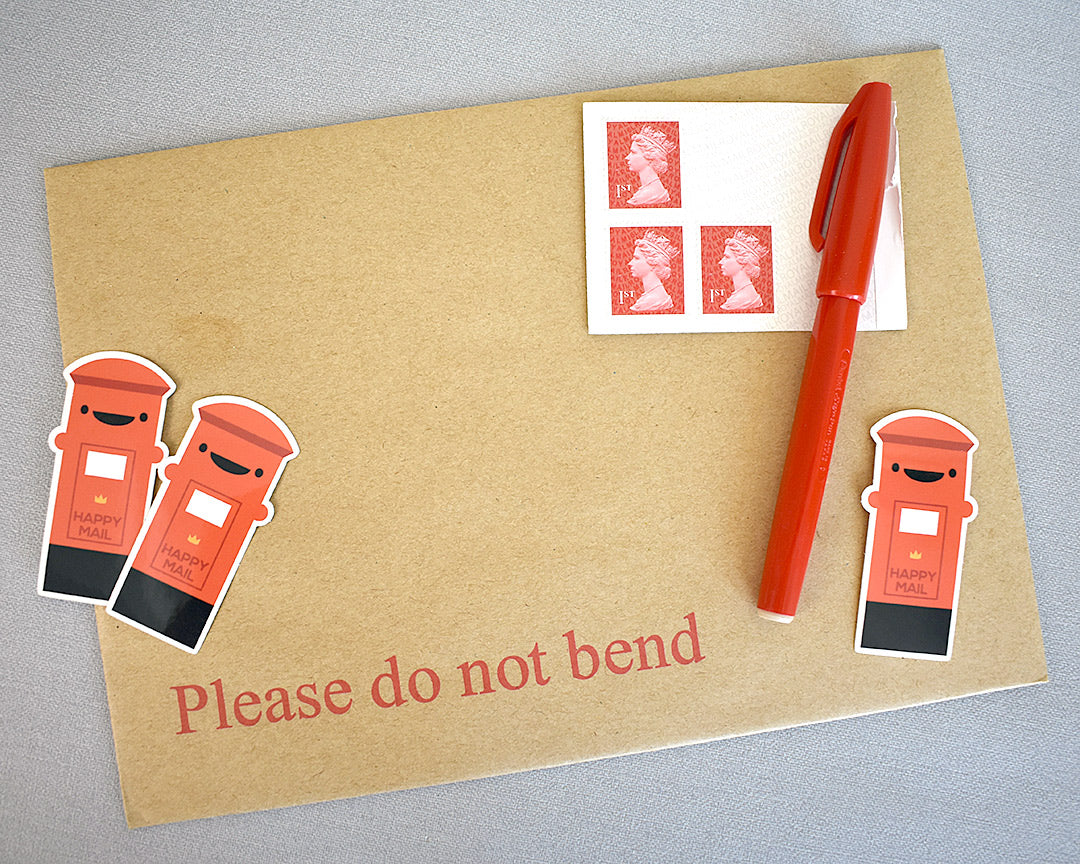 3 Postbox stickers displayed with an envelope, stamps and pen