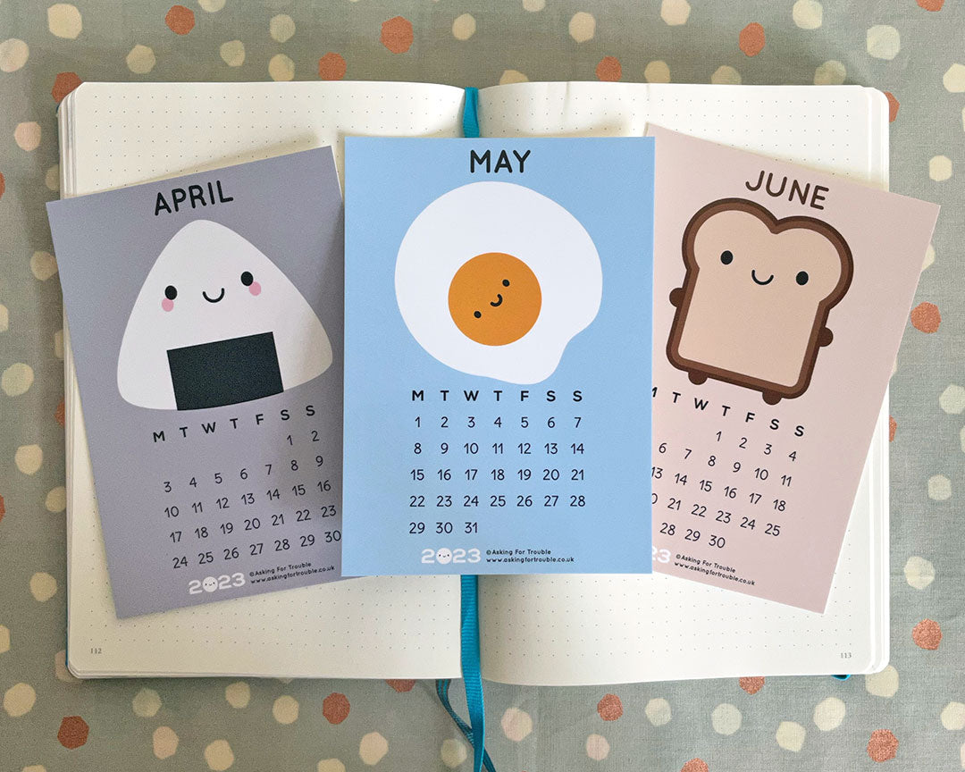 The April, May and June postcards on an open notebook