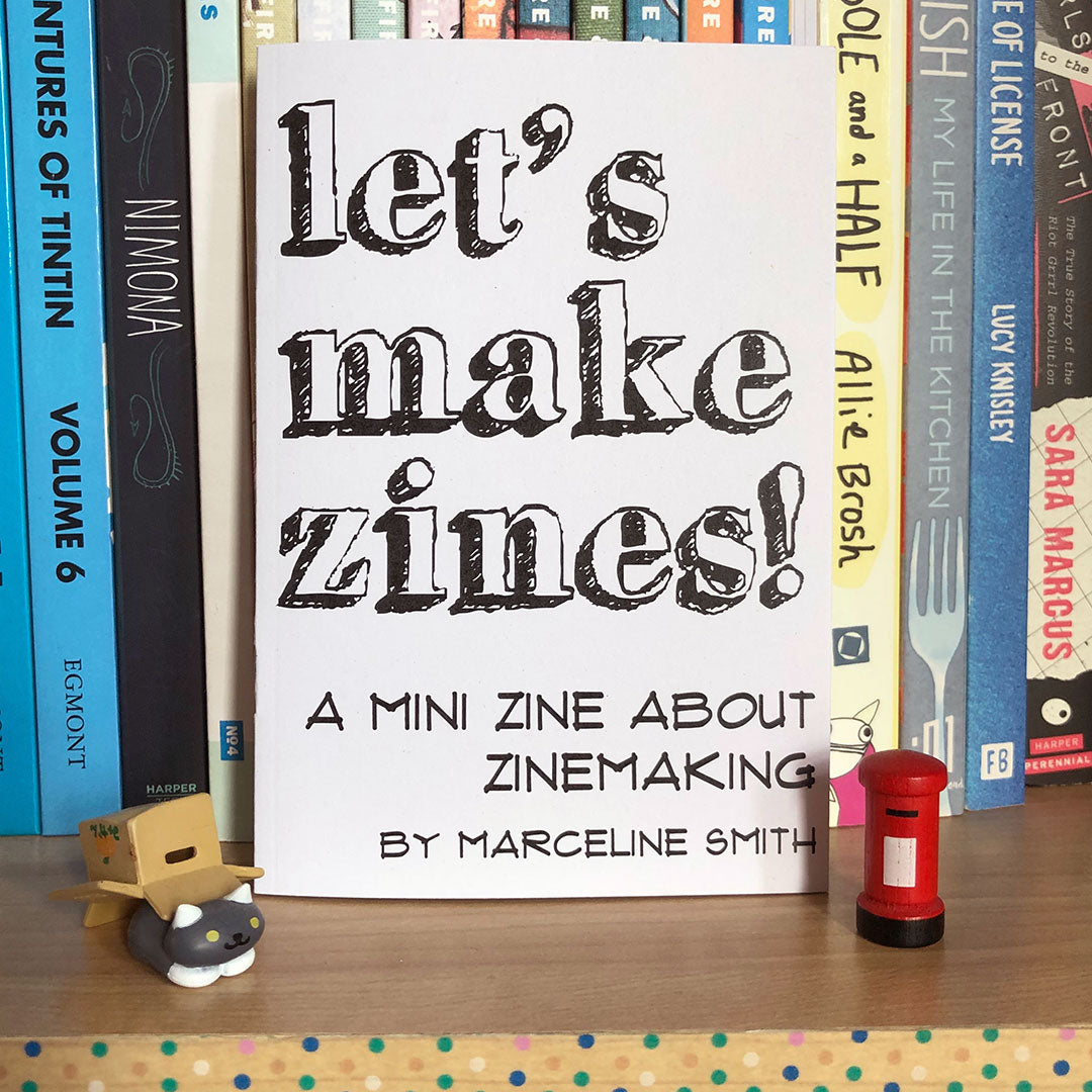 The zine propped up on a bookshelf with cute figures