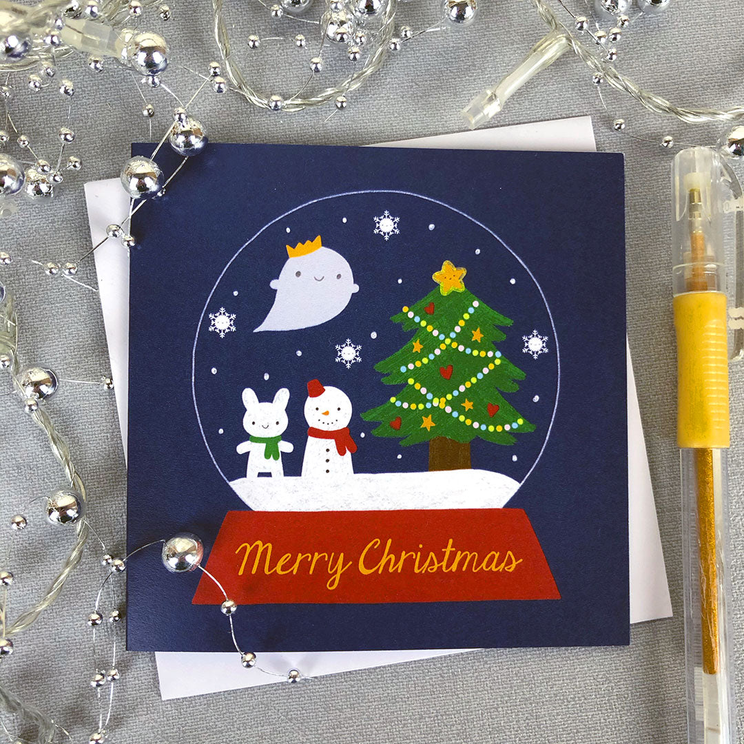 An illustrated card with a snowglobe filled with Christmas tree, snowmen and ghost plus the words Merry Christmas
