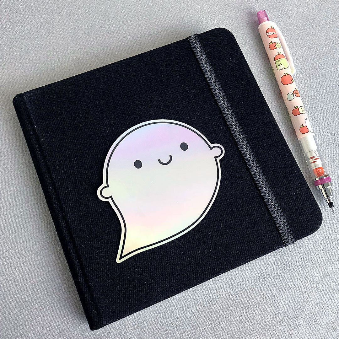 The vinyl sticker decorating a small sketchbook with pen for scale