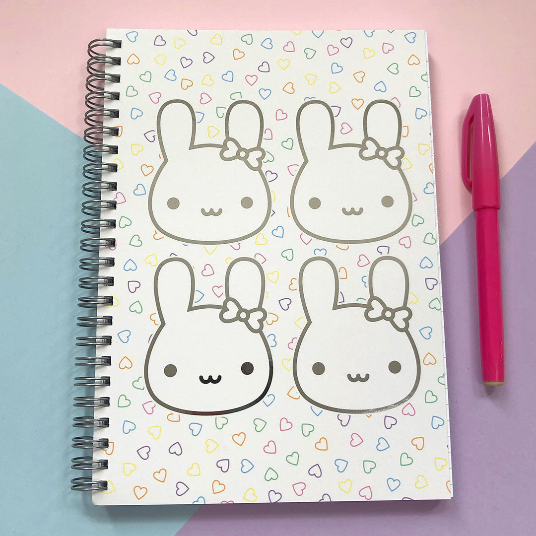 Spiral bound notebook with 4 kawaii bunny faces in silver mirror foil on a background of small scattered hearts
