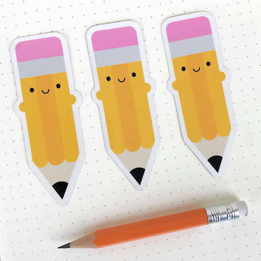 Three die cut vinyl stickers of a happy pencil, displayed on a notebook page with a real pencil