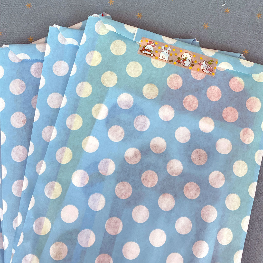 A stack of blue polka dot paper bags sealed with washi tape