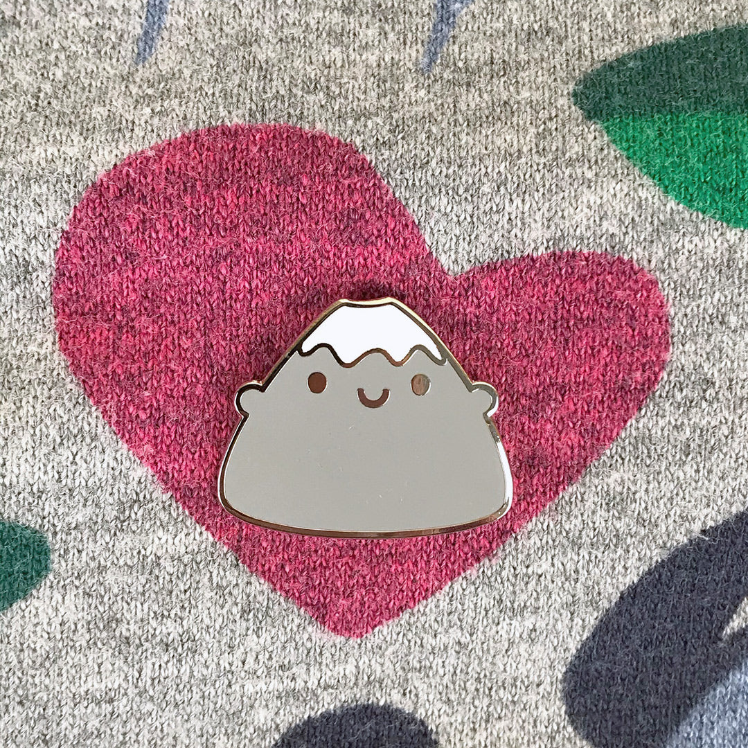 A happy snow-capped Mt Fuji enamel pin, pinned to a patterned jumper
